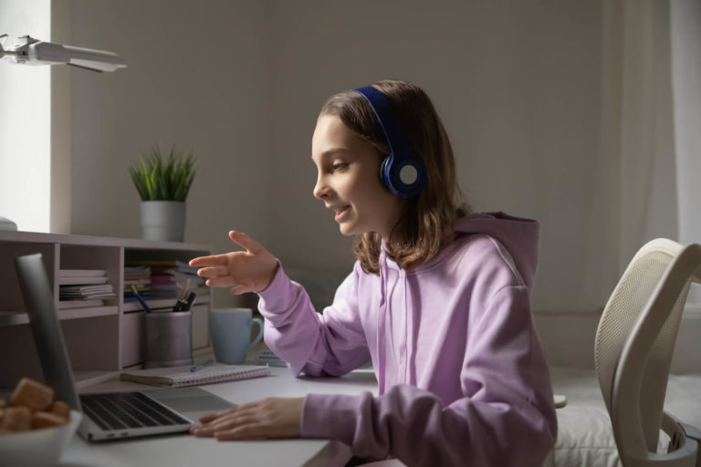 Young girl wearing headphone talking to an open laptop.