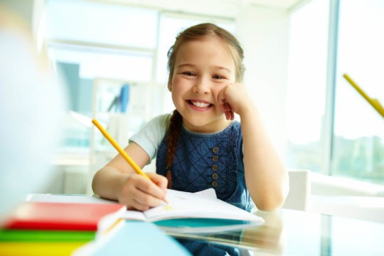 Young girl writing on paper at desk while smiling