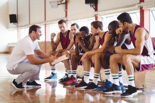 Coach kneeling while speaking to his diverse basketball team