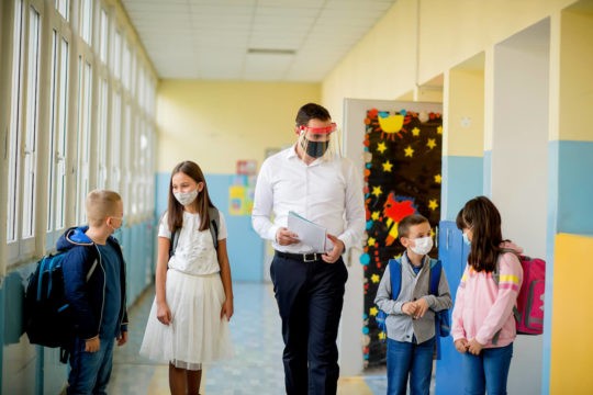 A teacher and a small group of students standing in a hallway wearing masks.