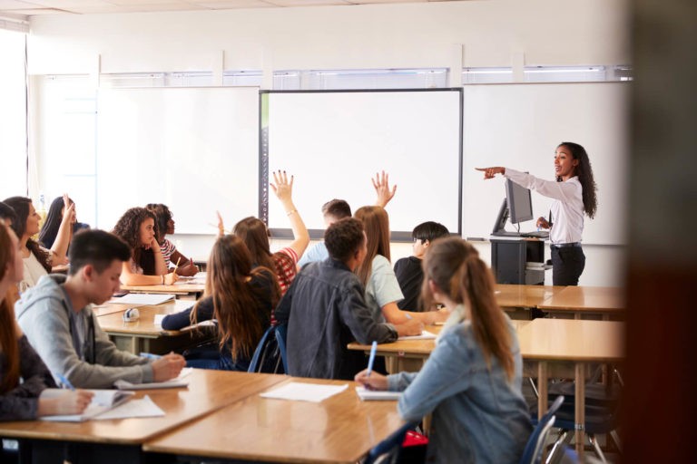 Teacher calling on students with their hands up in a classroom.