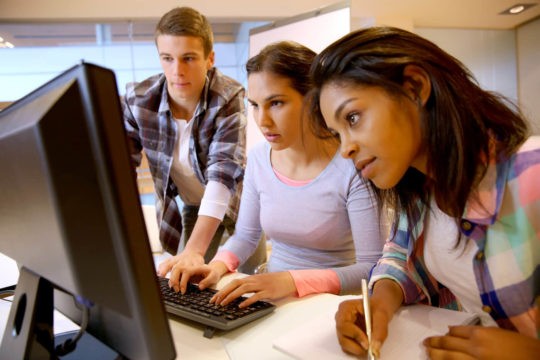 Three older students working together at a computer.