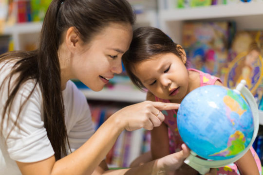 Asian teacher and young girl examining Asia on a globe.