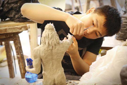 High school student working on a clay sculpture of a historical figure.