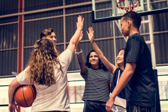 A group of young teens high fiving on a basketball court