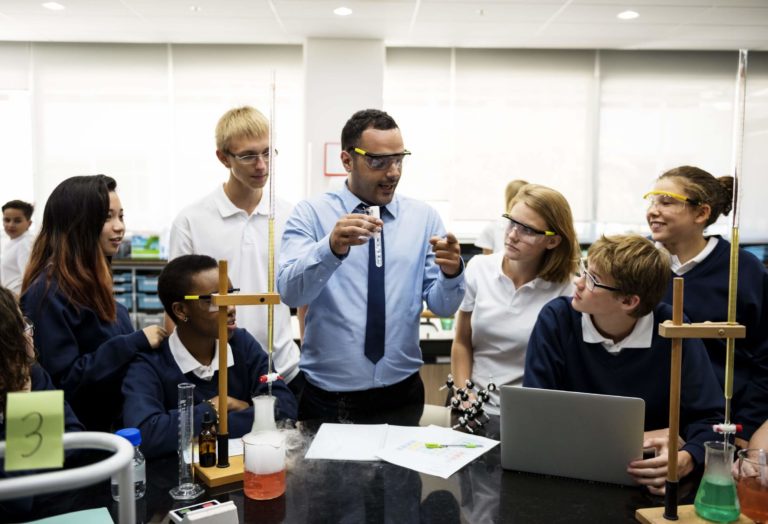Teacher demonstrating a chemistry experiment to a group of students in a classroom lab.