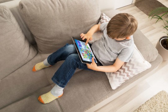 Kid sitting on couch playing a game on a tablet